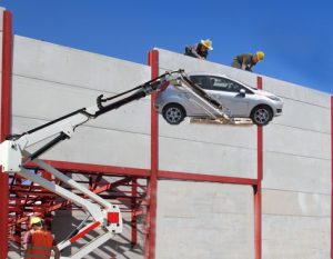 Workers hoist a Ford Fiesta over a simulated border wall. 